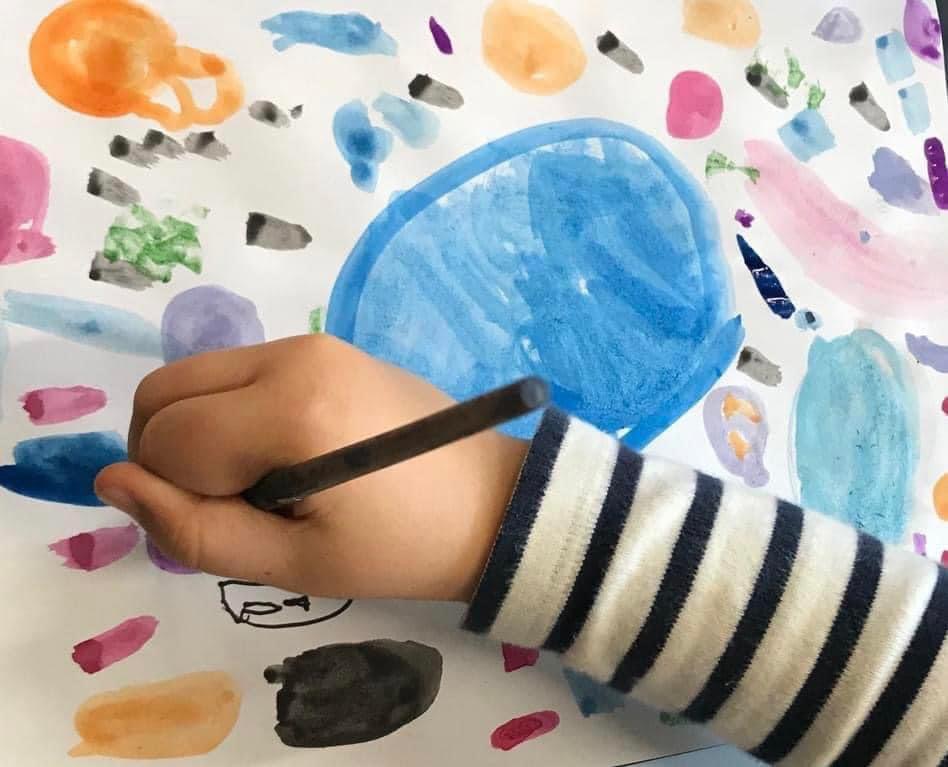 Child paints with watercolour. Image shows hand above circles of colour.
